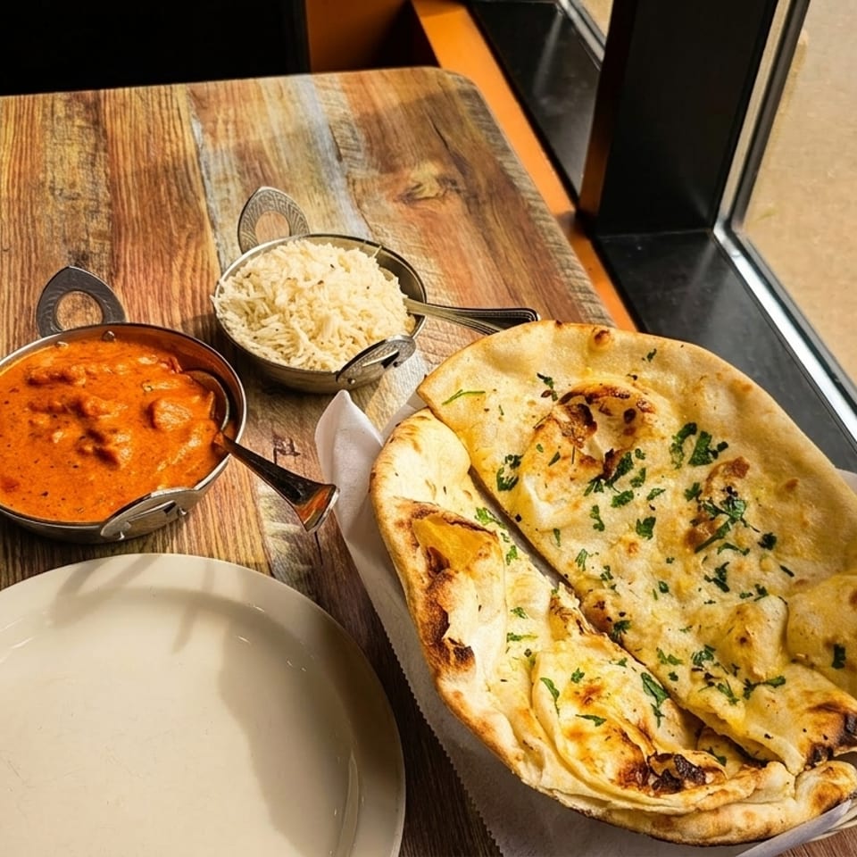 Indian meal with butter chicken, rice, and naan bread on a rustic wooden table.
