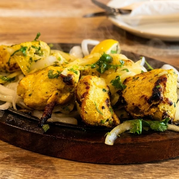 Sizzling chicken tikka with onions, cilantro, and lemon on a hot plate.