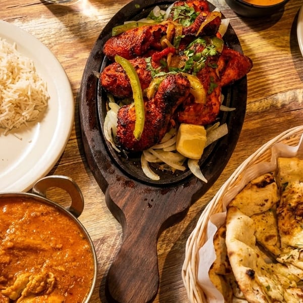 Overhead view of Indian dishes: chicken tikka, rice, curry, and naan bread on a wooden table.