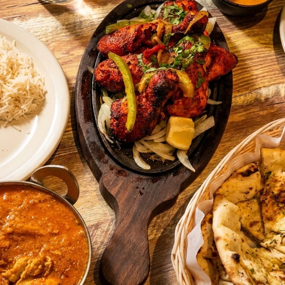 Overhead view of Indian dishes: chicken tikka, rice, curry, and naan bread on a wooden table.